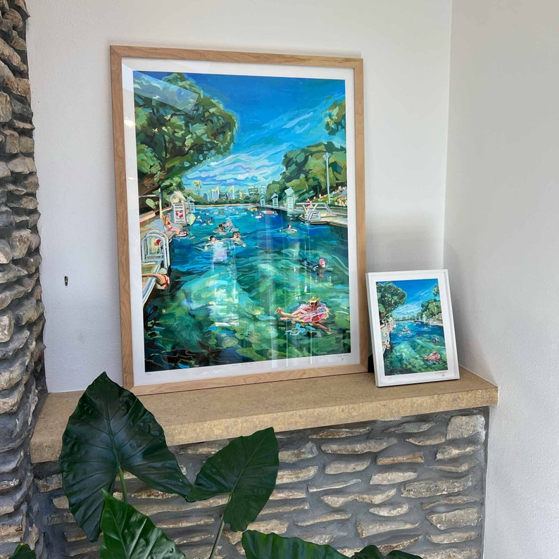 K&ouml;nnte beinhalten: Zwei gerahmte Kunstdrucke, die eine Schwimmbadszene mit schwimmenden und treibenden Personen zeigen. Der gr&ouml;&szlig;ere Druck ist in einem hellen Holzrahmen, der kleinere in einem wei&szlig;en Rahmen. Das Wasser ist klar t&uuml;rkis, mit gr&uuml;nen B&auml;umen und blauem Himmel.