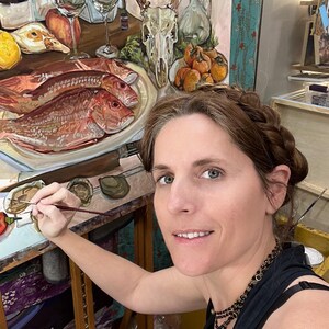 May include: A woman paints a still life on a canvas. The painting features a deer skull, fruit, and fish on a plate. The woman is wearing a black tank top and has her hair in a braid.