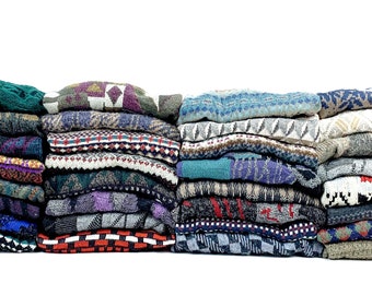 Può includere: Una grande pila di maglioni in maglia piegati che presentano una varietà di motivi geometrici, fair isle e astratti colorati. La collezione include diverse texture e tavolozze di colori, che vanno dai blu e verdi scuri ai rossi e bianchi vivaci.