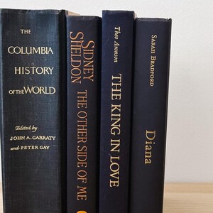 May include: Four hardcover books with dark blue covers and gold lettering. Titles include "The Columbia History of the World," "Sidney Sheldon The Other Side of Me," "The King in Love," and "Diana." The books are arranged vertically.