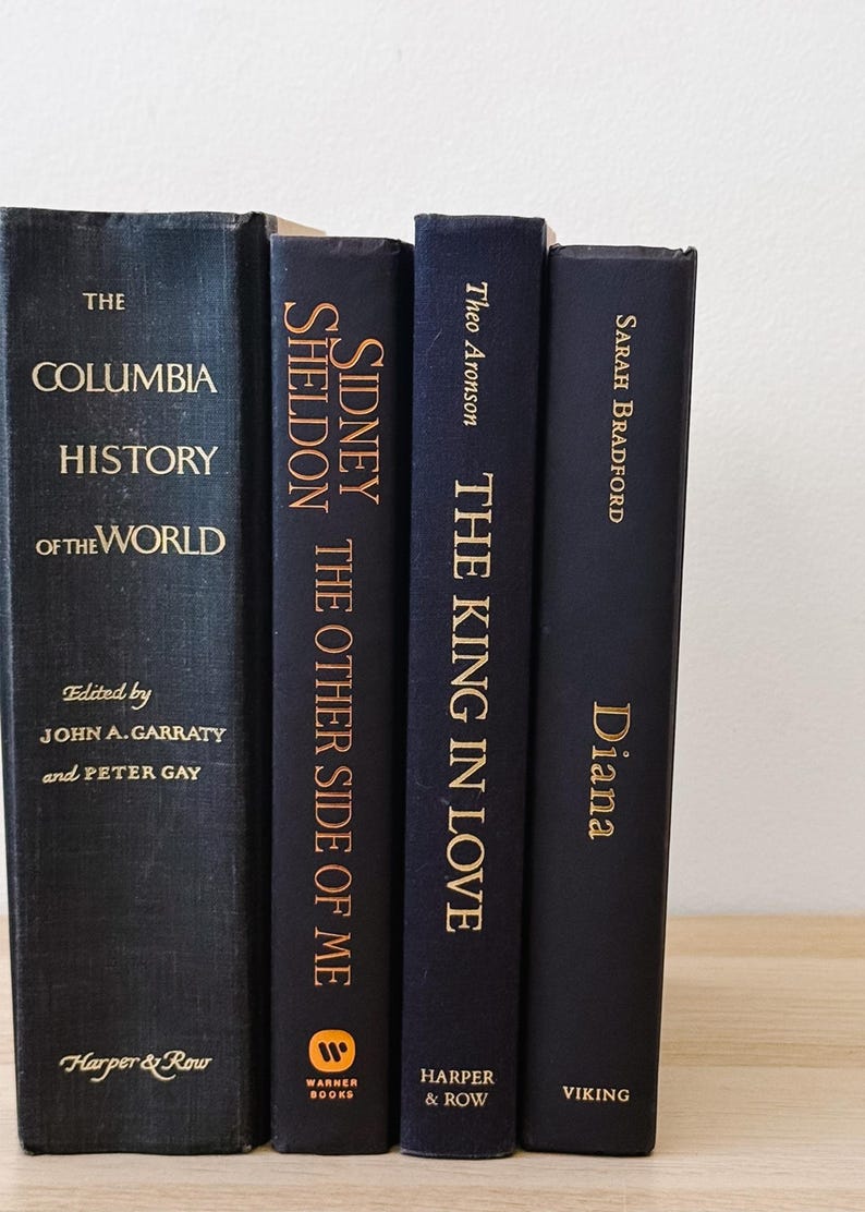 May include: Four hardcover books with dark blue covers and gold lettering. Titles include "The Columbia History of the World," "Sidney Sheldon The Other Side of Me," "The King in Love," and "Diana." The books are arranged vertically.