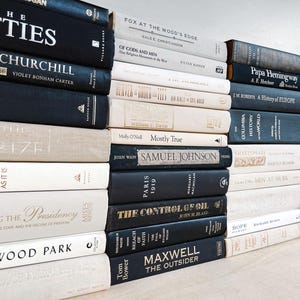 May include: A collection of hardcover books in various sizes and colors. The spines display titles like "The Fifties," "Hollywood Park," and "The Control of Oil." The books are stacked on a light-colored surface, creating a visually appealing arrangement.