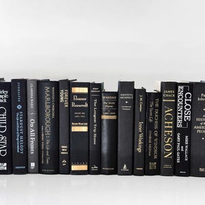 May include: A collection of hardcover books with black spines and various titles. The books are arranged in a row, with titles and author names visible. The spines have gold or white lettering. The books are on a white surface.