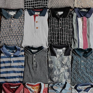 May include: A collection of twelve folded polo shirts arranged in a grid. The shirts feature various patterns including geometric shapes, stripes, plaid, paisley, and botanical prints in diverse colors such as blue, gray, black, red, and tan.