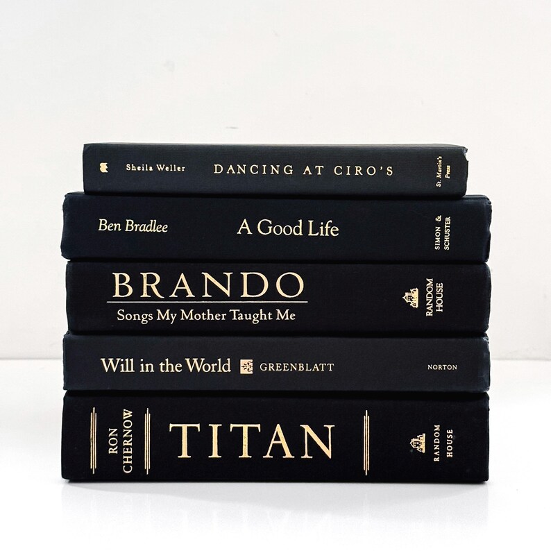 May include: A stack of five hardcover books with black covers and gold lettering. Titles include "Dancing at Ciro's," "A Good Life," "Brando," "Will in the World," and "Titan." The books are arranged vertically against a white background.
