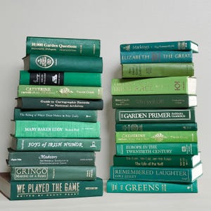 May include: Two vertical stacks of hardcover books in various shades of green. The left stack includes titles like 10,000 Garden Questions and Gringo, while the right stack features Markings, The Garden Primer, and The Greens, among other titles.
