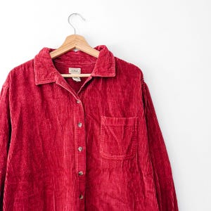 May include: A long-sleeved button-down shirt made of red corduroy fabric. The shirt features a classic collar, a single chest pocket on the left side, and a row of matching red buttons down the front. The interior label reads L.L.Bean.