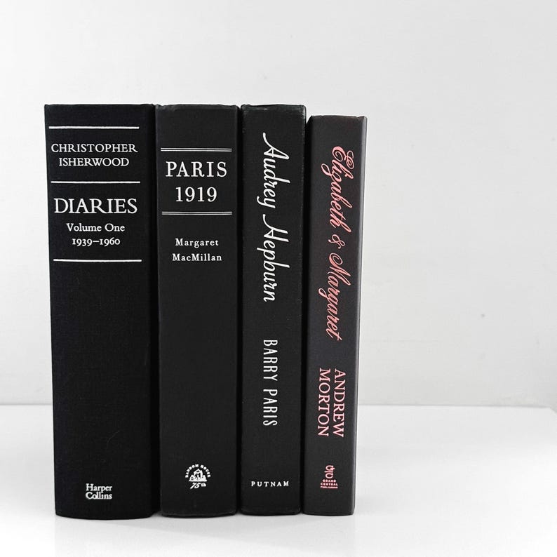 May include: Four hardcover books with black covers. The books are titled "Diaries Volume One 1939-1960", "Paris 1919", "Audrey Hepburn", and "Elizabeth & Margaret". The titles and author names are in white and pink.