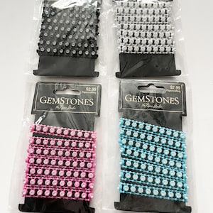 Könnte beinhalten: Vier Rollen Strassbesatz in Schwarz, Weiß, Rosa und Blau. Jede Rolle ist in einer durchsichtigen Plastiktüte mit einer schwarzen Karte verpackt, auf der "Gemstones The Paper Studio" und "Papercrafting" steht.