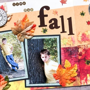 Puede incluir: Una página de álbum de recortes con un tema otoñal. La página presenta dos fotos de un niño pequeño de pie junto a un árbol, un reloj y varias hojas de otoño. El texto "time for fall" está escrito en la página.
