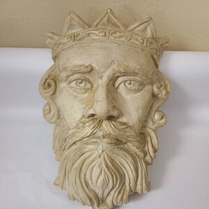 May include: A beige plaster sculpture of a king's face with a crown. The sculpture has a detailed beard and mustache.
