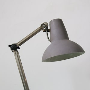 May include: A vintage silver and grey adjustable desk lamp with a black base. The lamp has a flexible arm and a grey metal shade.