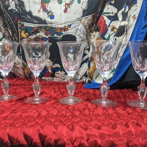 May include: Five clear glass wine glasses with a cut crystal design. The glasses are arranged in a row on a red velvet surface.