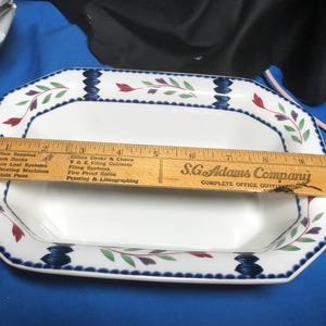 May include: White octagonal serving dish with a blue and white border and a floral design in red, green, and purple. The dish is sitting on a blue surface.