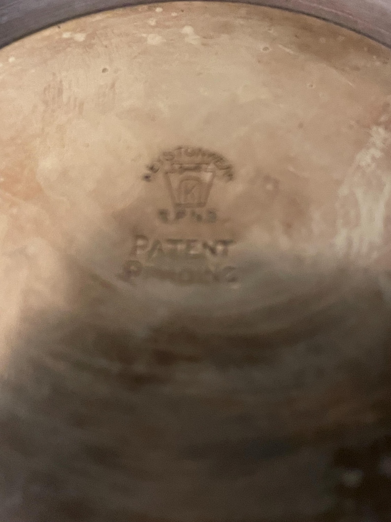 May include: Close-up of a ceramic object with a light brown interior and a darker rim. The centre features embossed text that reads "KEYSTONE" above a logo and the words "PATENT PENDING".