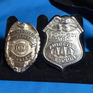 May include: Two silver badges with black backing. The left badge says "Detective Target Stores State of Missouri". The right badge says "School Boy Patrol Auto Club AAA Missouri".
