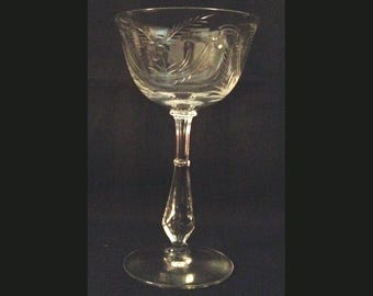 May include: A clear glass stemmed coupe with a delicate etched floral design. The glass has a tall, slender stem and a wide, shallow bowl.