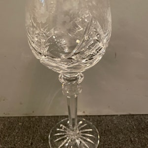 May include: A clear crystal wine glass with a cut design. The glass has a tall stem and a round base.