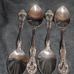May include: Four silver spoons with ornate handles. The spoons have a polished finish and are arranged in a row.