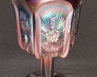 May include: A iridescent purple glass goblet with a thistle design. The goblet has a wide bowl and a tall stem with a flared base.