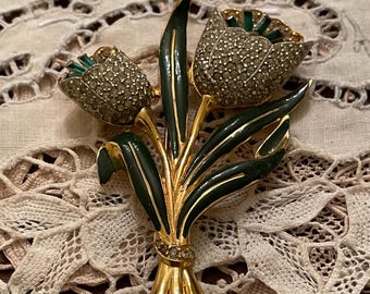 May include: A vintage brooch in the shape of a bouquet of tulips. The brooch features gold-tone metal, dark green enamel leaves, and tulip heads encrusted with clear rhinestones. A small cluster of rhinestones secures the bouquet.