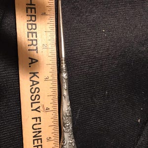 May include: A silver shoe horn with an ornate handle. The handle is about 5 inches long.