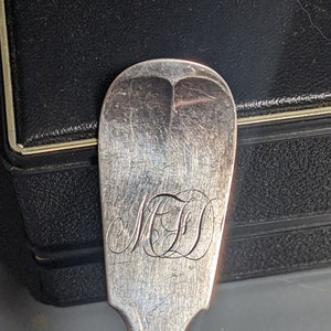 May include: Close-up of a silver spoon with a monogrammed "MFD" on the handle.
