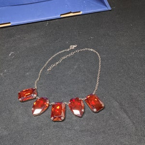 May include: A silver chain necklace with five large, faceted, red gemstone pendants.