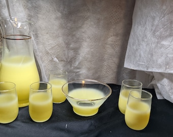 Könnte beinhalten: Ein Set aus sechs gefrosteten Gläsern und einem Krug, gefüllt mit einer gelben Flüssigkeit, sowie eine gefrostete Glasschüssel, alles auf einer schwarzen Oberfläche.