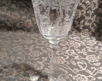 May include: A clear, etched glass with a floral design. The glass has a long stem and a wide bowl. The etched design includes flowers and other decorative elements. The glass is likely used for serving wine or other beverages.