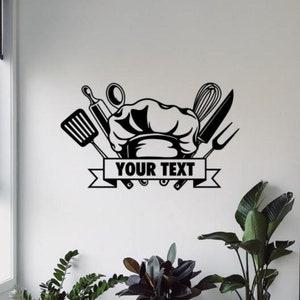 May include: Black and white kitchen wall decal featuring a chef's hat, cooking utensils, and a banner with the text "YOUR TEXT".