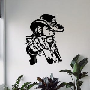 Pode incluir: Arte de parede em preto e branco de um homem com um chapéu de cowboy apontando. O chapéu tem um design de caveira e ossos cruzados. O homem tem bigode e cabelo comprido. A imagem é um estilo de silhueta.