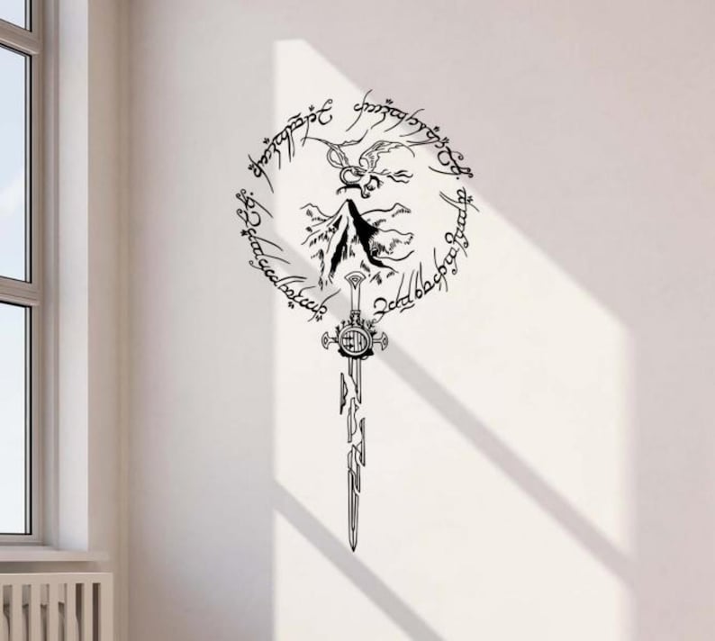 May include: Black wall decal featuring a sword design with a circular inscription and a mountain silhouette. The design is a stylized representation of a fantasy theme, suitable for home decor.