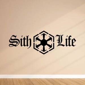 Puede incluir: Adhesivo de pared negro "Sith Life". El texto está en una fuente gótica, con un símbolo geométrico en el centro. El adhesivo está sobre una pared beige con suelo de madera.