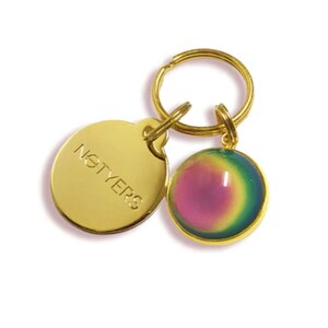 May include: Gold keychain with a round, iridescent charm and a round tag with the word "NOTYERS" engraved on it.