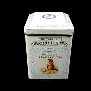 Puede incluir: Una lata blanca con ribetes azules que muestra el texto "The World of Beatrix Potter" y "Traditional English Breakfast Tea". La lata tiene una imagen de un conejo sosteniendo una taza de té.