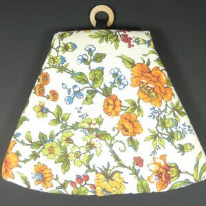 Puede incluir: Una pantalla de lámpara cónica de tela blanca con un patrón floral en tonos naranja, amarillo, verde y azul. La pantalla tiene un anillo de madera en la parte superior.