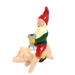 Könnte beinhalten: Eine rote und grüne Gnome-Figur, die auf einem rosa Schwein reitet. Der Gnome hält ein silbernes und graues Objekt in der Hand.