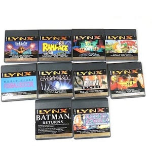 May include: A collection of ten black and gold Lynx video game cartridges. The cartridges feature various game titles, including "Rampage", "World Class Fussball Soccer", "Cyberball", "Block Out", "Deform", "Power Factor", "Batman Returns", "Jahido", "Tournament Cyberball", and "Sega Games".