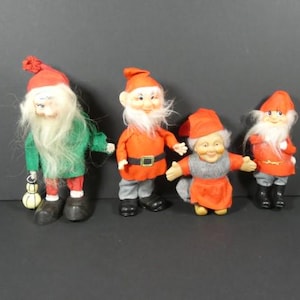 Puede incluir: Cuatro muñecos de gnomo de Navidad vintage con sombreros y atuendos rojos y verdes. Los gnomos están hechos de tela y tienen barbas blancas.