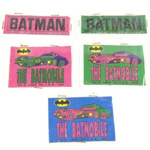 May include: Four stickers featuring the Batmobile and Batman logos. The stickers are pink, green, blue, and white. The text on the stickers reads "The Batmobile" and "Batman".