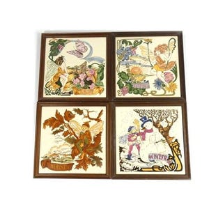 May include: A set of four square wall tiles in dark brown wooden frames, each featuring a seasonal illustration. The tiles depict a fairy in spring, a fairy in summer, a fairy in autumn with the text HERBST, and a snowman in winter with the text WINTER.