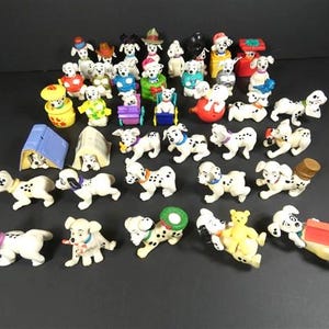 Könnte beinhalten: Eine Sammlung von Dalmatiner-Hundefiguren in verschiedenen Posen und Outfits. Die Figuren sind weiß mit schwarzen Flecken und verfügen über Accessoires wie Hüte, Schleifen und Spielzeug. Einige befinden sich in Miniaturhäusern oder mit anderen Figuren.