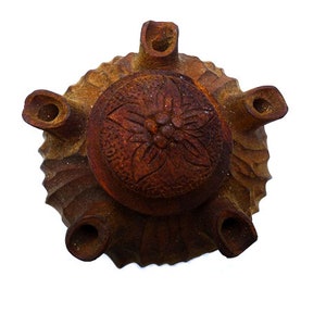 May include: A terracotta brown ceramic pot with a carved floral design on the lid. The pot has six spouts around the rim.