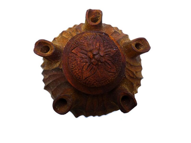 May include: A terracotta brown ceramic pot with a carved floral design on the lid. The pot has six spouts around the rim.