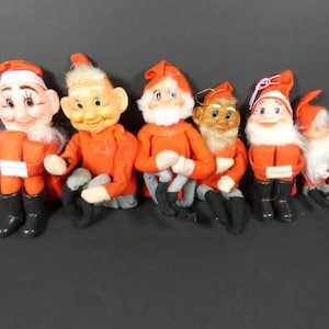 May include: Set of seven vintage felt Christmas elves with red and white outfits. The elves have different facial expressions and are wearing hats.