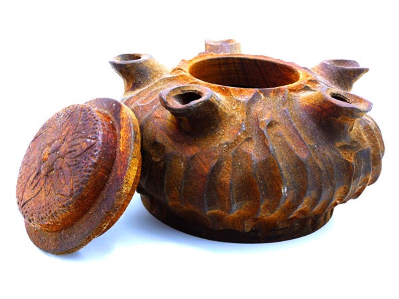 May include: A rustic brown ceramic pot with a lid, featuring a textured, wavy design. The pot has five openings around the top, and the lid has a raised, circular design.
