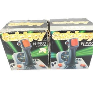 Puede incluir: Dos mandos de juego Quickjoy N-Pro negros y grises para juegos de Nintendo en su embalaje original. Las cajas son negras con detalles en amarillo y verde. Los joysticks son negros con botones rojos.