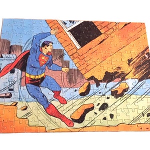 May include: A vintage jigsaw puzzle featuring a comic book illustration of Superman flying through the air, breaking through a brick wall. The puzzle is made of cardboard and has a colorful design.
