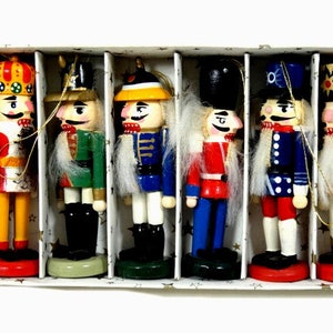 May include: Set of six wooden nutcracker ornaments. Each nutcracker is painted in different colors and designs, including red, blue, yellow, and green. The nutcrackers are all wearing hats and have facial features.